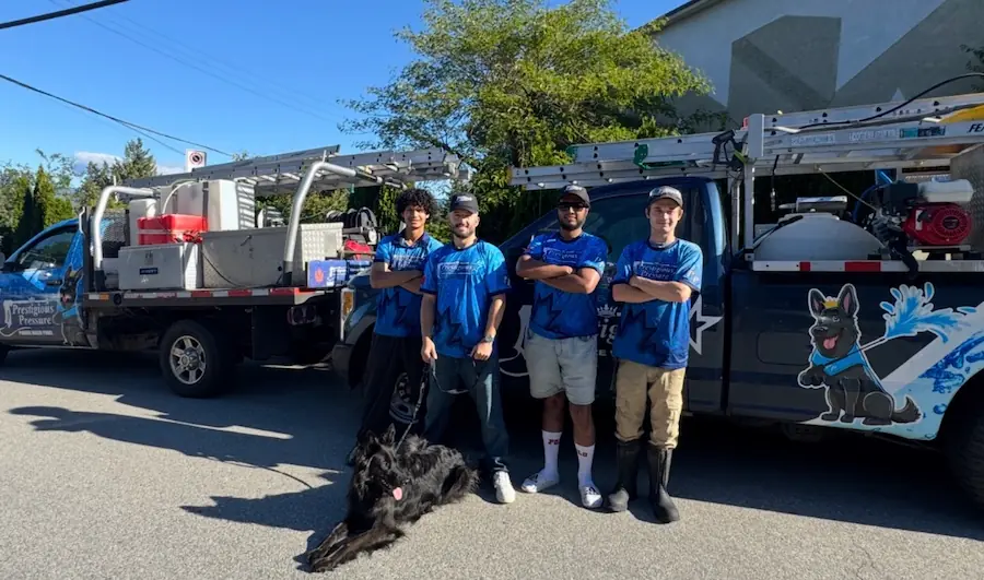The Prestigious Pressure Washing crew in branded shirts, standing between two of the company's work trucks